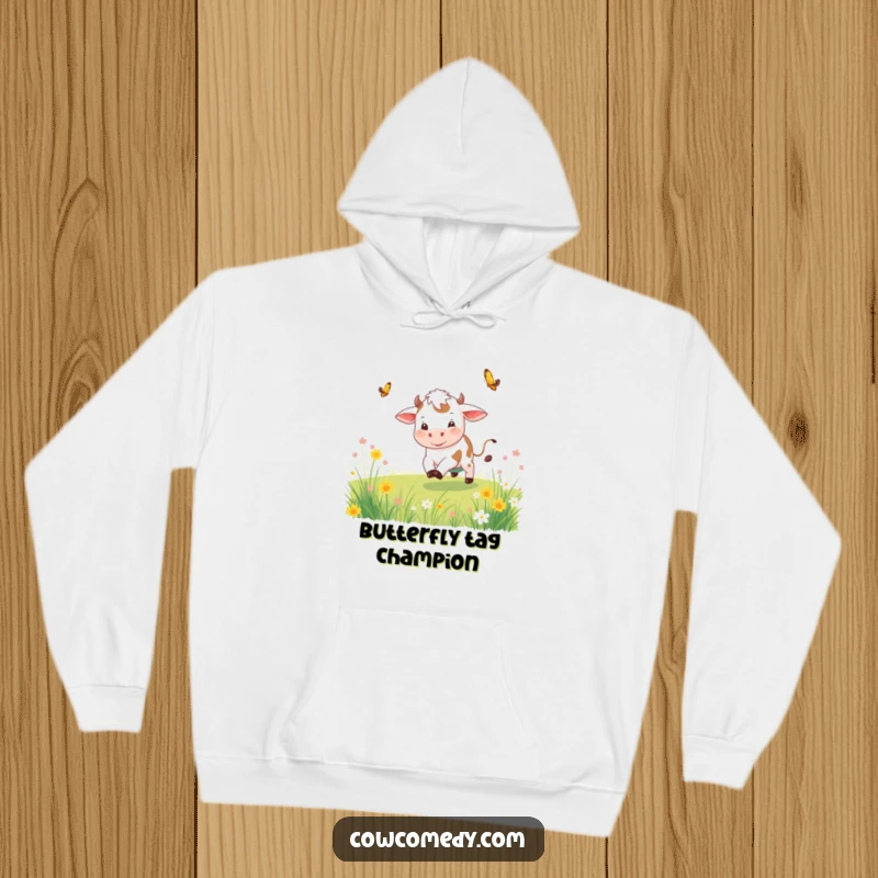 Funny playful cow hoodie depicting a cow chasing a butterfly through a meadow, radiating happiness and movement.