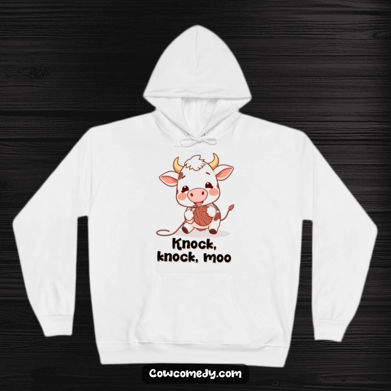 Funny hoodie design depicting an elated cow using its nose to playfully bat a ball of yarn, capturing a moment of pure, unadulterated fun.